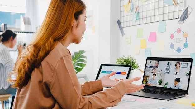 Asia businesspeople using laptop talk to colleagues discussing business brainstorm about plan in video call meeting in new normal office. Free Photo