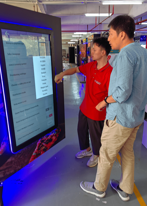 The pizza vending machine’s head engineer explains to HI-COM’S project manager how to configure the machine’s settings using the touch screen. The pizza vending machine’s head engineer explains to HI-COM’S project manager how to configure the machine’s settings using the touch screen.